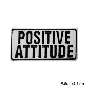 May include: A rectangular white patch with a black border and the words "POSITIVE ATTITUDE" in bold black letters. The patch measures 9.5cm x 4.5cm.
