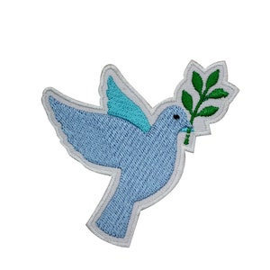 May include: Embroidered patch featuring a light blue dove carrying a green olive branch. The dove has a light blue wing and is outlined in white. The patch is designed for application on clothing or accessories.