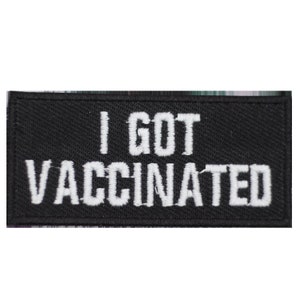 May include: A black rectangular patch with white embroidered text. The text on the patch reads "I GOT VACCINATED". The patch is likely made of fabric and designed to be sewn or ironed onto clothing or accessories.