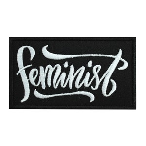 Peut inclure: Patch brodé blanc sur fond noir avec le mot "féministe" dans une police d'écriture cursive stylisée.