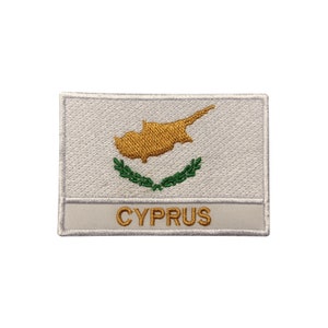 May include: White embroidered patch with the flag of Cyprus. The flag features a yellow outline of the island of Cyprus on a white background with a green olive branch wreath below. The word "CYPRUS" is written in gold below the flag.
