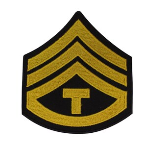 May include: A gold embroidered military rank patch with three stripes and a 'T' in the center on a black background.