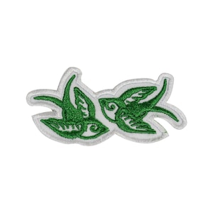 May include: Green embroidered patch featuring two stylised swallows facing each other. The swallows are outlined in white.