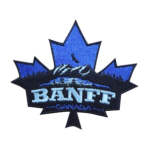 May include: Blue and black embroidered patch shaped like a maple leaf with the text "BANFF CANADA" and a mountain range with a crescent moon in the background.