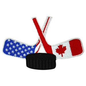 May include: An embroidered patch featuring two crossed hockey sticks, one with the American flag and the other with the Canadian flag, with a black hockey puck in the center.