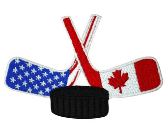 May include: An embroidered patch featuring two crossed hockey sticks, one with the American flag and the other with the Canadian flag, with a black hockey puck in the center.