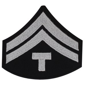 May include: A black fabric patch with two silver chevron stripes and a silver letter "T" in the centre.