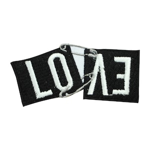 May include: Black fabric patch with white embroidered letters spelling "LOVE" in a broken, overlapping design.