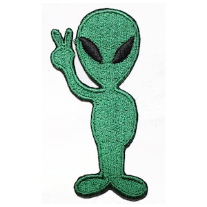 May include: Green alien with black eyes giving the peace sign. The alien is embroidered on a fabric patch.