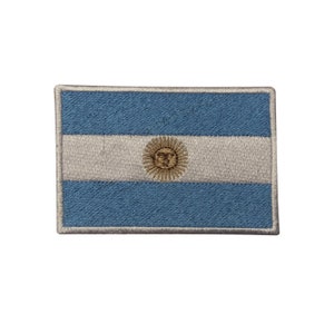 May include: Embroidered patch featuring the flag of Argentina. The design includes a light blue background with a central white stripe and a golden sun emblem. The patch has a rectangular shape with a stitched border.