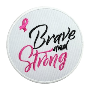 May include: White round embroidered patch with a pink ribbon and the text "Brave and Strong" in black and pink lettering.