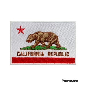 Könnte beinhalten: Weißer gestickter Aufnäher mit der Flagge des US-Bundesstaates Kalifornien. Er zeigt einen roten Stern, einen braunen Bären, der auf einem grünen Feld geht, und die Worte "CALIFORNIA REPUBLIC" in braunen Buchstaben. Der Aufnäher ist 9 cm x 6 cm groß.
