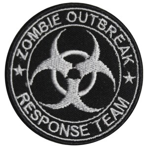 May include: A black and white embroidered patch featuring a biohazard symbol and the text "Zombie Outbreak Response Team".