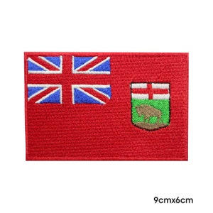 May include: Red embroidered patch with the Canadian flag and the coat of arms of Manitoba. The flag features a Union Jack in the upper left corner. The coat of arms features a buffalo and a red cross on a green background. The patch measures 9 cm by 6 cm.