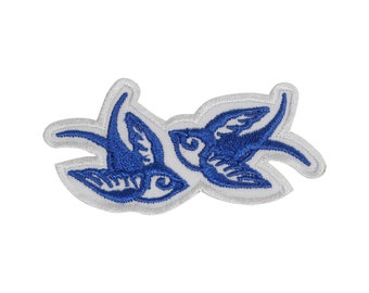 May include: Blue embroidered patch with two stylized swallows facing each other. The patch is on a white background.