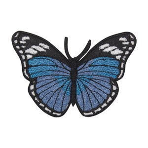 May include: An embroidered butterfly patch in blue and black. The butterfly has a dark blue body and wings with a lighter blue gradient. The wings have a white outline.
