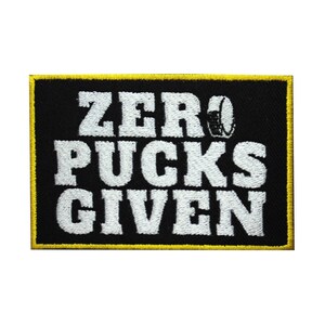 May include: A rectangular black patch with a yellow border. The patch features the white text "ZERO PUCKS GIVEN" with a hockey helmet graphic. The patch is designed for apparel or accessories.
