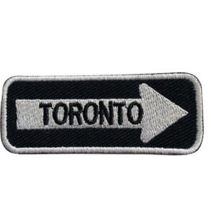 May include: Black and white embroidered patch with a white arrow pointing to the right and the word "TORONTO" in black.