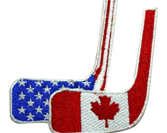 May include: Two embroidered hockey stick patches. One features the American flag with blue, white, and red colors. The other patch displays the Canadian flag with a red maple leaf on a white background.