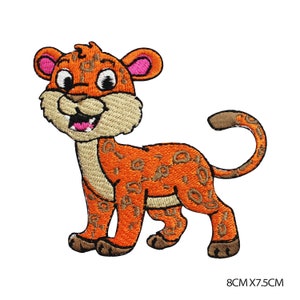 May include: Embroidered patch featuring a cartoon leopard cub in orange with brown spots. The cub has a tan face, pink ears, and a smiling expression. The patch measures 8cm x 7.5cm.
