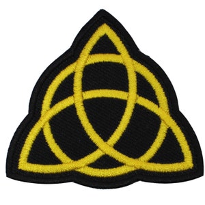 May include: A yellow embroidered patch with a black background featuring a triquetra symbol, a three-pointed knot.