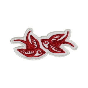 May include: Red embroidered patch with two stylized birds flying in opposite directions. The birds are outlined in white and have white wings.