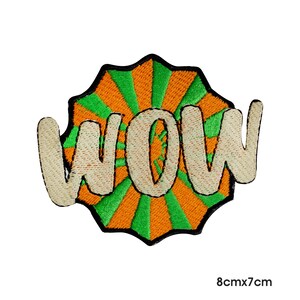 May include: An embroidered iron-on patch with a green and orange sunburst design and the word "WOW" in white.