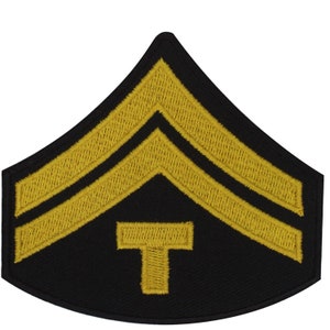 May include: A black and gold military rank patch with two gold chevrons and a gold T in the centre.