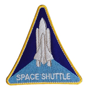 May include: A blue and white embroidered patch shaped like a triangle with a white space shuttle in the centre and the words "SPACE SHUTTLE" at the bottom.