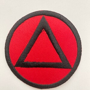 May include: A red and black embroidered patch with a black triangle inside a circle.