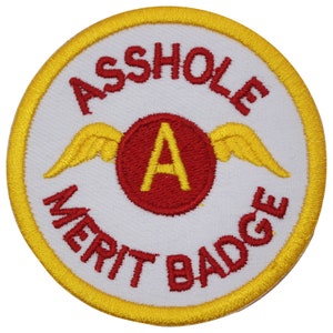 May include: A white round patch with a yellow border. The patch has red text that reads "ASSHOLE MERIT BADGE" and a red circle with a yellow "A" inside. The circle has yellow wings on either side.