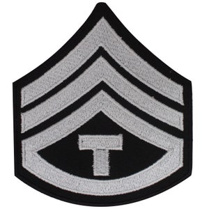 May include: A black and silver military rank patch with three silver chevrons and a silver T in the center.