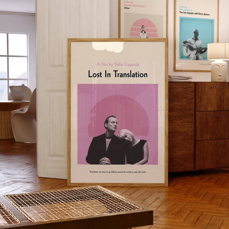 May include: A movie poster for the film "Lost in Translation" directed by Sofia Coppola. The poster features a pink background with a large circle in the center. Two people are standing in front of the circle, a man and a woman, with the woman leaning her head on the man's shoulder. The text "A film by Sofia Coppola" and "Lost in Translation" are printed in white on the poster. The quote "Sometimes you have to go halfway around the world to come full circle" is printed at the bottom of the poster.