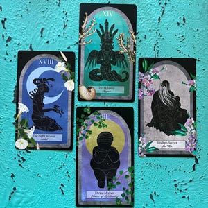 May include: Four tarot cards with black borders and illustrations. The cards feature images of figures, moons, and botanical elements. Text on the cards includes "The Night Weaver", "The Alchemy", "Divine Mother", and "Wisdom Keeper". The background is a textured turquoise surface.