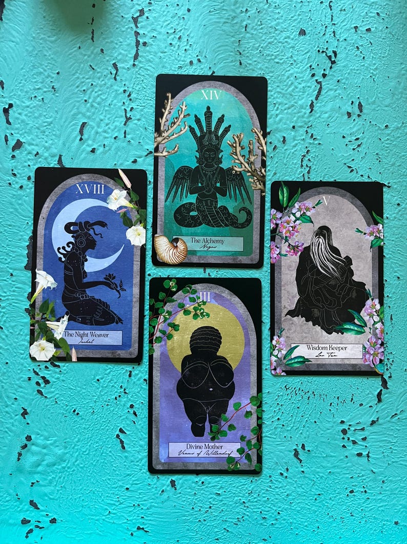 May include: Four tarot cards with black borders and illustrations. The cards feature images of figures, moons, and botanical elements. Text on the cards includes "The Night Weaver", "The Alchemy", "Divine Mother", and "Wisdom Keeper". The background is a textured turquoise surface.