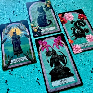 May include: Four tarot cards with black illustrations on a teal background. The cards feature images of a cat, a figure, a squirrel, and a deity, each with floral and botanical elements. The cards are labelled with numbers and suit names.