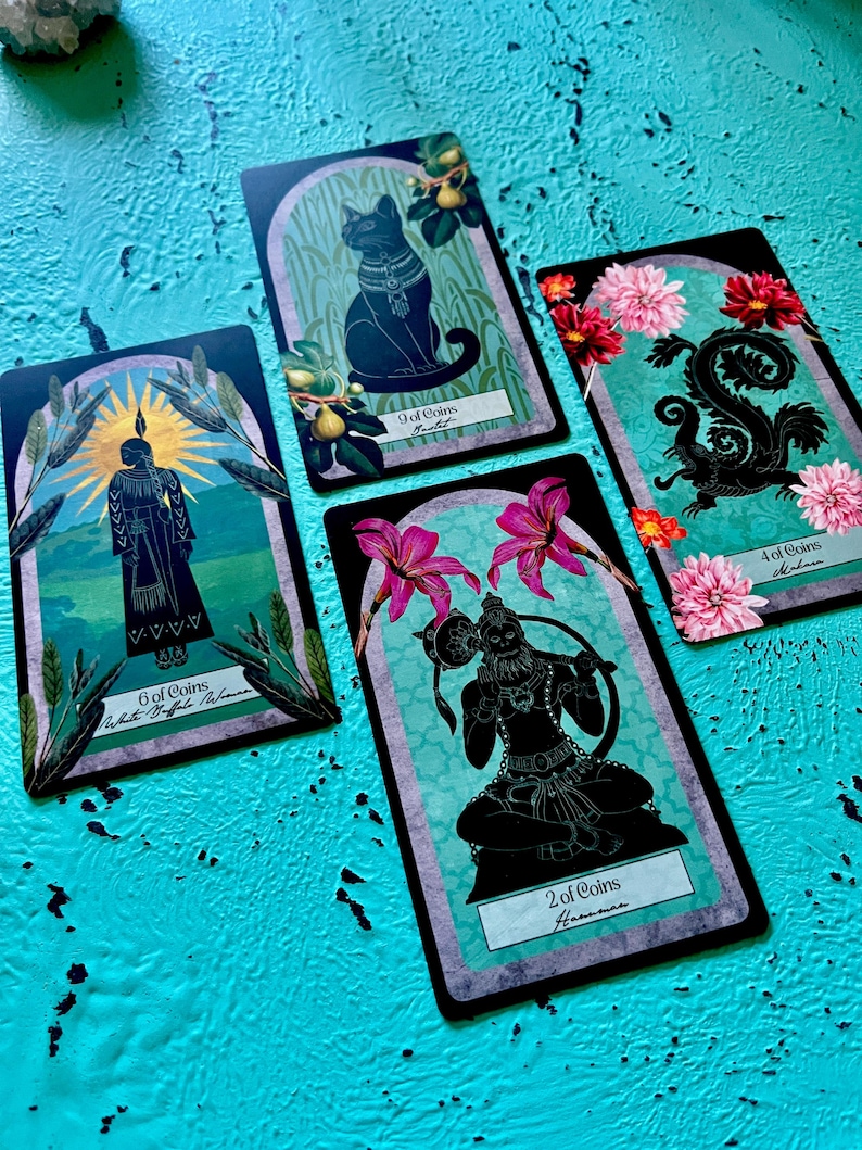 May include: Four tarot cards with black illustrations on a teal background. The cards feature images of a cat, a figure, a squirrel, and a deity, each with floral and botanical elements. The cards are labelled with numbers and suit names.