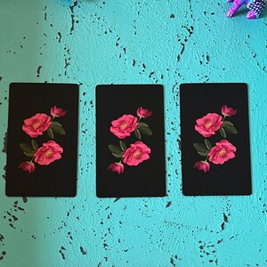May include: Three black rectangular cards with a floral design. Each card features a vibrant pink rose with green leaves. The roses are in full bloom, with detailed petals. The cards are arranged vertically against a textured turquoise background.