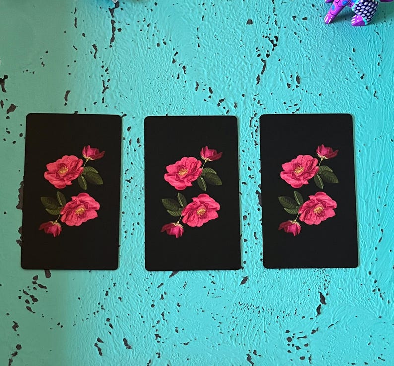 May include: Three black rectangular cards with a floral design. Each card features a vibrant pink rose with green leaves. The roses are in full bloom, with detailed petals. The cards are arranged vertically against a textured turquoise background.