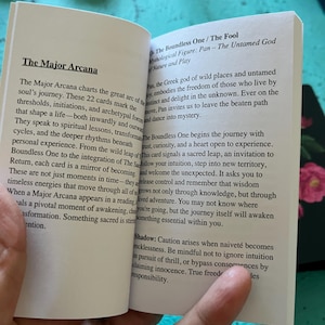 May include: An open book with text about "The Major Arcana" and "The Boundless One / The Fool" tarot card. The text explains the card's meaning, focusing on spiritual lessons and personal growth. The book is held open, revealing the pages.