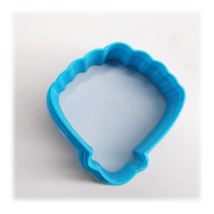 May include: A blue plastic cookie cutter shaped like a seashell. The cutter is designed to create a seashell-shaped cookie.