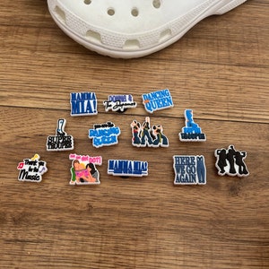 Puede incluir: Un conjunto de 10 abalorios coloridos para zapatos con varias referencias musicales y de la cultura pop. Los abalorios incluyen im&aacute;genes de cantantes y bandas, como Mamma Mia, ABBA y Donna and the Dynamos. Los abalorios tambi&eacute;n incluyen texto como "Dancing Queen", "Super Trouper" y "Here We Go Again".