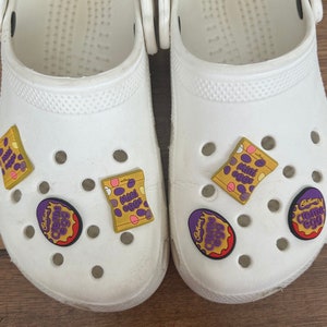 May include: White clogs with purple, yellow and red Cadbury Creme Egg Jibbitz charms. The charms feature the Cadbury Creme Egg logo and the words "Cadbury Creme Egg" and "Mini Eggs".