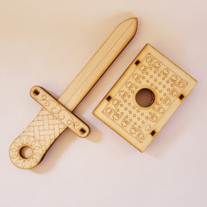 sword through finger magic trick. A plywood laser cut device.  Wooden hand held box decorated as the King of hearts playing card. A finger is pushed through a hole in the box.  A small wooden sword is then pushed into the box and out the other side