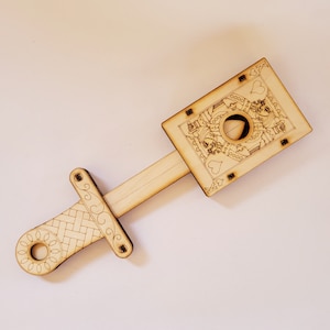 sword through finger magic trick. A plywood laser cut device.  Wooden hand held box decorated as the King of hearts playing card. A finger is pushed through a hole in the box.  A small wooden sword is then pushed into the box and out the other side
