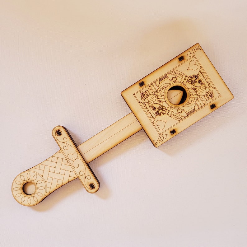 sword through finger magic trick. A plywood laser cut device.  Wooden hand held box decorated as the King of hearts playing card. A finger is pushed through a hole in the box.  A small wooden sword is then pushed into the box and out the other side