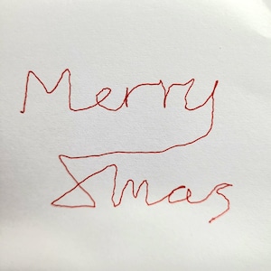 May include: A white surface featuring the handwritten text Merry Xmas in red ink. The letters are formed with a single continuous line style, creating a casual and handwritten appearance across two lines of text on the plain white background.