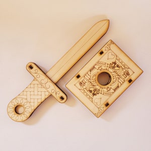 sword through finger magic trick. A plywood laser cut device.  Wooden hand held box decorated as the King of hearts playing card. A finger is pushed through a hole in the box.  A small wooden sword is then pushed into the box and out the other side