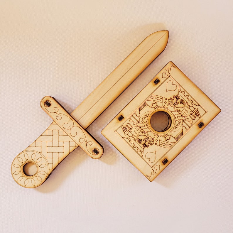 sword through finger magic trick. A plywood laser cut device.  Wooden hand held box decorated as the King of hearts playing card. A finger is pushed through a hole in the box.  A small wooden sword is then pushed into the box and out the other side