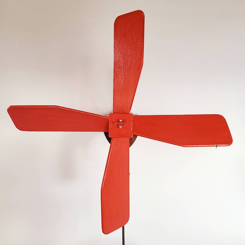 May include: A red four-bladed wind spinner with a metal centre piece. The blades are made of wood and are painted a bright red colour.